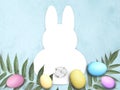 Mock up Easter flat lay with bunny template frame, colored eggs, leaves and cotton flower on blue background.