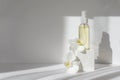 Mock-up of glass bottle with essential oil stands on white geometric 3d podium in rays of sunlight, surrounded by orchid Royalty Free Stock Photo