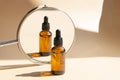 Mock up of glass dropper bottle is reflected in mirror in rays of sunlight. Close-up, beige background. Concept of body