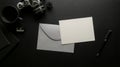 Mock-up greeting card with grey envelope on dark office desk with digital camera and office supplies Royalty Free Stock Photo