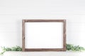 Mock up A4 horizontal frame made of rough wood with on a shelf with greens