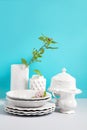 Mock up image with white Crockery,dish, utensils and flower vases on grey table against blue background with space for design.