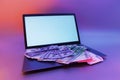 Mock up laptop with white screen and bundles of dollars and euros against a background of colorful bright neon UV blue and purple Royalty Free Stock Photo