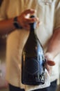 Mock up of large dark glass champagne bottle. Empty black sticker. Chilled bottle of wine in the hands of the waiter in beige