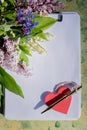 Mock up letter about love.Red wooden heart lies on blank white paper on a wooden table with spring flowers, a greeting Royalty Free Stock Photo