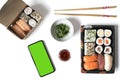 Mock up mobile with green screen on a white table with sushi food in take-away containers