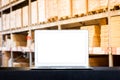 Mock up of modern computer or laptop with blank screen on table with Blurred boxes on rows of shelves in warehouse