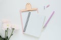 mock up of an open notebook on a spring, pink clipboard, pen, paper clip and three chrysanthemum flower on a white table.