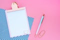 Mock up pink clipboard, pen, paper clip and blue striped paper on a pink background.