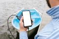 Mock-up of a smartphone with charging from Power bank in a man`s hand. Against the background of a boat on the water at the woode