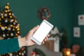 Mock up, smartphone in the girl`s hand. against the background of the New Year and Christmas interior with a Christmas tree, a Royalty Free Stock Photo