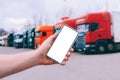 Mock up a smartphone in the hand of a man. Against the background of red trucks. Logistics concept Royalty Free Stock Photo