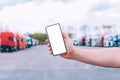 Mock up a smartphone in the hand of a man. Against the background of red trucks. Logistics concept.