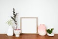 Mock up square wood frame with home decor, plants and branches. Wooden shelf against a white wall.