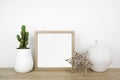 Mock up square wood frame with modern home decor on a wood shelf against a white wall