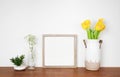 Mock up square wood frame with succulent and spring flowers. Wooden shelf against a white wall.