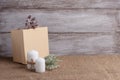 mock-up of two white candles in a jute rope and beige gift box, cones, sprig of lichen yagel on a wooden background
