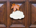 Mock up, welcome empty table sign of cloud shape decorated with orange maple leaf hanging on dark wooden entrance door.