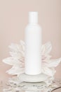 Mock up of white bottle lotion bottle with white flower, stone and mirror on beige background.