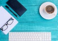 Mock up of white cup of coffee, white keyboard, black notebook, black pen, black glasses and white empty sheet on turquoise wood d Royalty Free Stock Photo