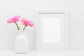 Mock up white frame and pink daisy flowers in vase against white wall on shelf Royalty Free Stock Photo