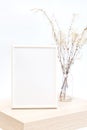 Mock up of a white photo frame in a minimalistic interior with a bouquet of pampas grass in a glass vase against a white wal