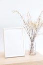 Mock up of a white photo frame in a minimalistic interior with a bouquet of pampas grass in a glass vase against a white wal