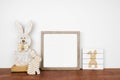 Mock up wood frame with Easter decor on a wood shelf. Square frame against a white wall.