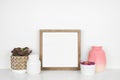 Mock up wood square frame with pink hue decor on a white shelf against a white wall