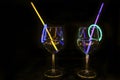 Mocktail wine glass filled with illuminated refreshing alcohol liquid and colorful straw with black background for nightlife party