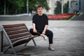 Mockup of a black casual t-shirt on a guy sitting on a blurred background of a park, on a bench, front view, for design