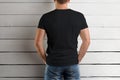 Mockup of a black t-shirt on a strong man holding his hands in the front pocket of jeans on a wooden background.