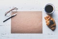 Mockup blank craft sheet of blank craft paper, pen, eye glasses and morning coffee cup with croissant on white wooden Royalty Free Stock Photo