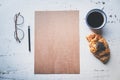 Mockup blank craft sheet of blank craft paper, pen, eye glasses and morning coffee cup with croissant on white wooden Royalty Free Stock Photo