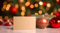 Mockup blank gold paper note greeting card, space for text with red baubles and gift box on blurry Christmas tree background, Royalty Free Stock Photo