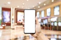 Mockup blank white screen mobile phone hand holding smartphone  with blurred image hall of ticket sales counter at movie theater. Royalty Free Stock Photo
