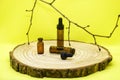 Mockup of brown glass vials with dropper lid on wooden board. Empty glass bottles with pipette, tree branch on yellow background.