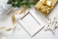 Mockup Christmas white frame with tree and golden ribbon and a gift, flatlay on a white wooden background, with place