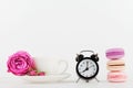 Mockup of coffee cup with rose flower, macaroon and alarm clock on white desk with clean space for text and design your blogging.