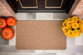 Mockup of a coir doormat before the house door, with autumn flowers and pumpkins