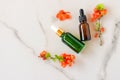 Mockup cosmetic face serum brown glass bottle with a pipette on a marble background with orange flowers. Female beauty concept, Royalty Free Stock Photo