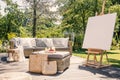 Mockup of easel on wooden terrace with rattan table and settee in the garden. Real photo