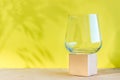 Mockup. Empty transparent glass on a textured cube on a beige surface on a yellow background with shadows from plants Royalty Free Stock Photo