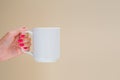 Mockup female hand with red manicure nails holds white ceramic mug isolated on beige. Copy space for text or your logo Royalty Free Stock Photo