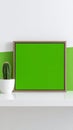 Mockup frame with green screen next to cactus pot, white shelf and white and green wall for display. Royalty Free Stock Photo