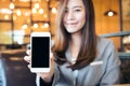 Asian beautiful business woman holding and showing white mobile phone with blank black screen and smiley face in cafe Royalty Free Stock Photo