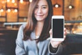 Asian beautiful business woman holding and showing white mobile phone with blank black screen and smiley face in cafe Royalty Free Stock Photo