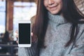 Mockup image of an Asian beautiful woman holding and showing white mobile phone with blank black screen in cafe Royalty Free Stock Photo