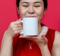 Mockup Image of an Asian Woman Drinking on a Blank Mug With Christmas Attire on a Red Background Royalty Free Stock Photo