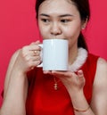 Mockup Image of an Asian Woman Drinking on a Blank Mug With Christmas Attire on a Red Background Royalty Free Stock Photo